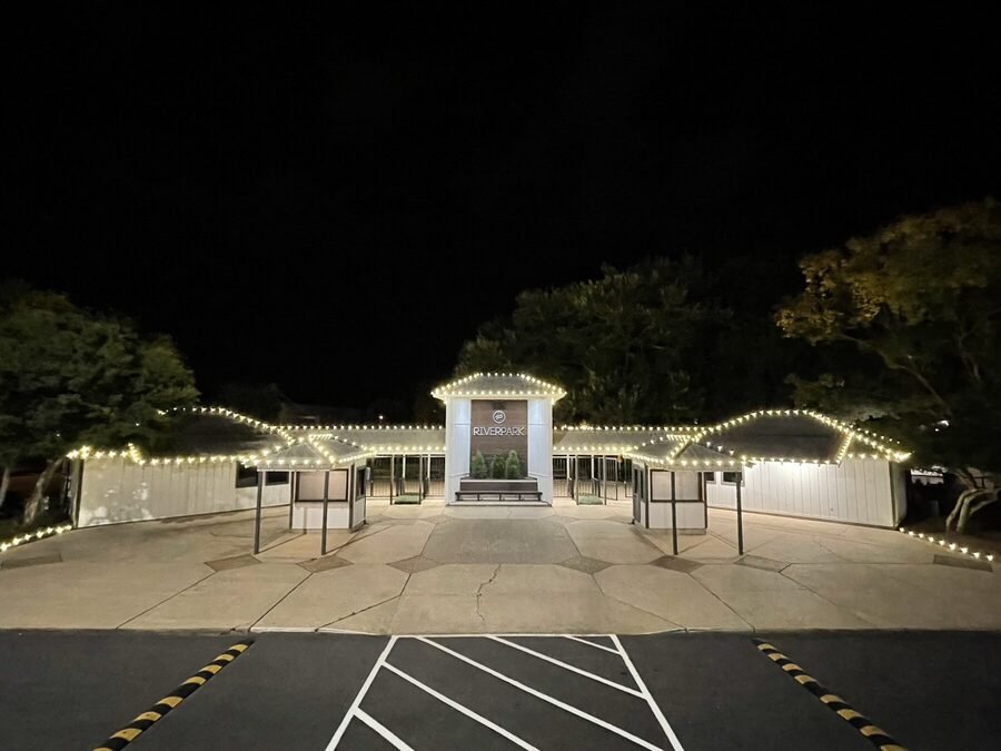 A clubhouse roofline outlined in warm white C9 bulbs at night, with the entrance canopy lit below.