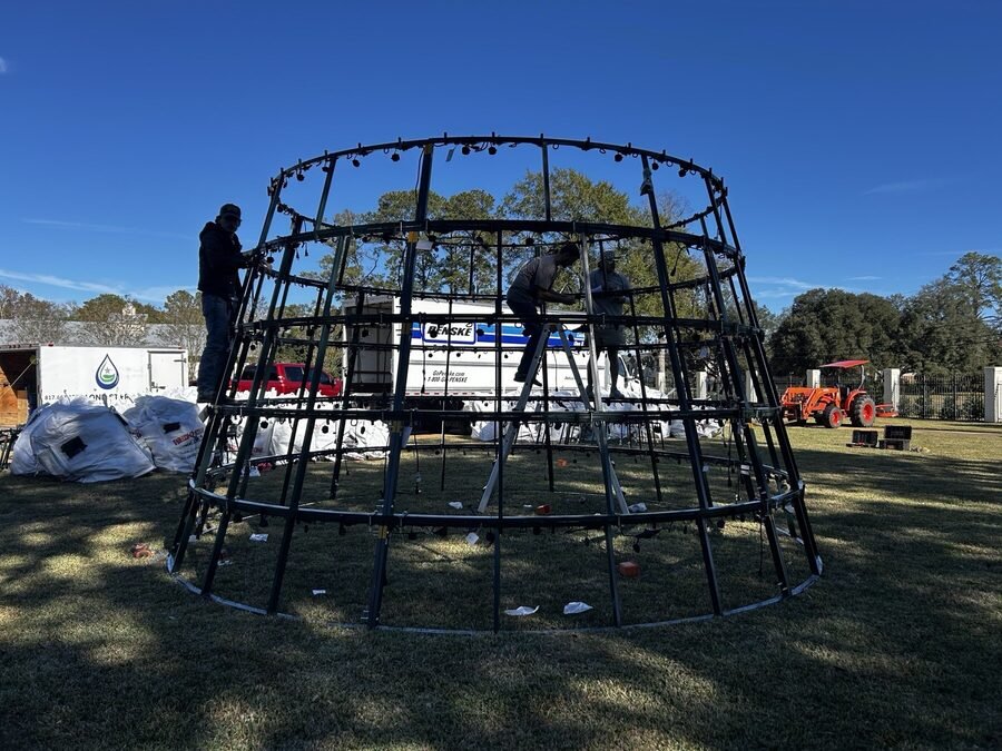 The steel ring frame of a commercial Christmas tree part way through assembly on a lawn in daylight.