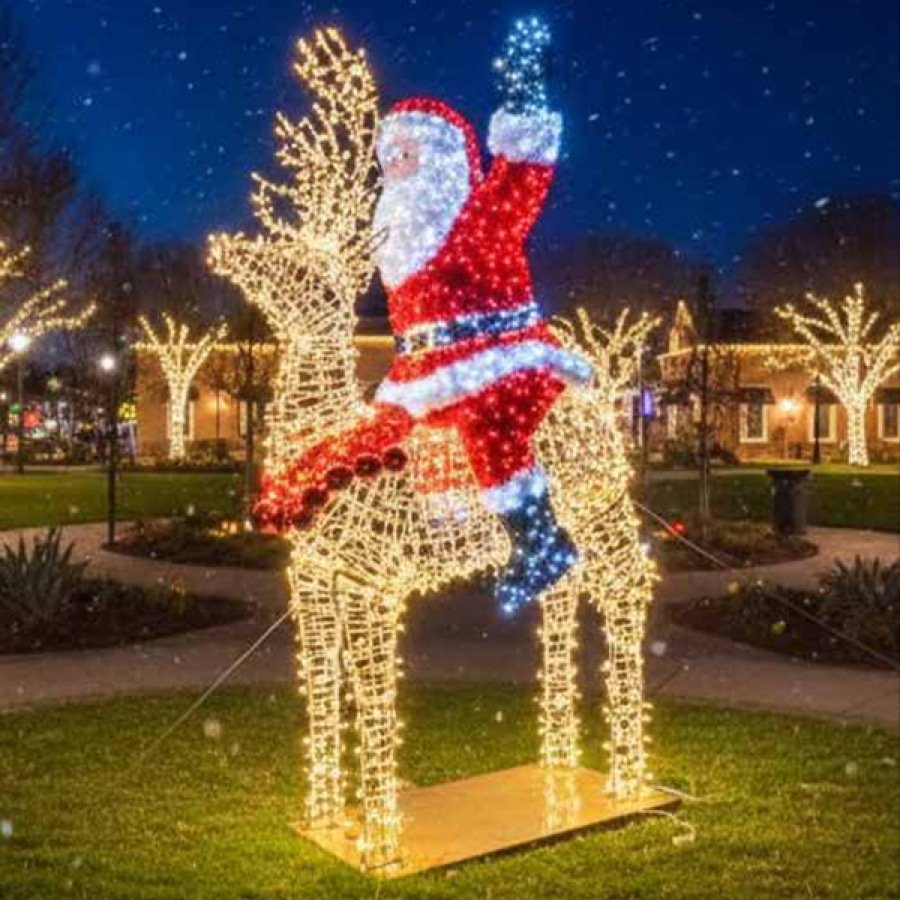 An illuminated Santa riding a stag, mounted above a lit walkway at night.