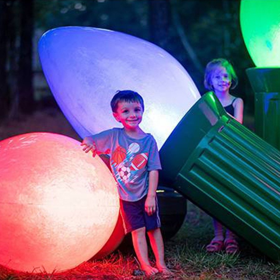 A child beside color changing oversized fiberglass Christmas bulbs.