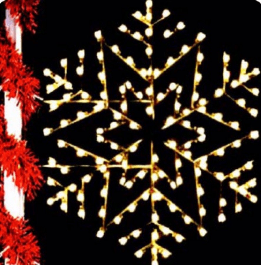 A lit red and gold snowflake mounted on a street pole at night.