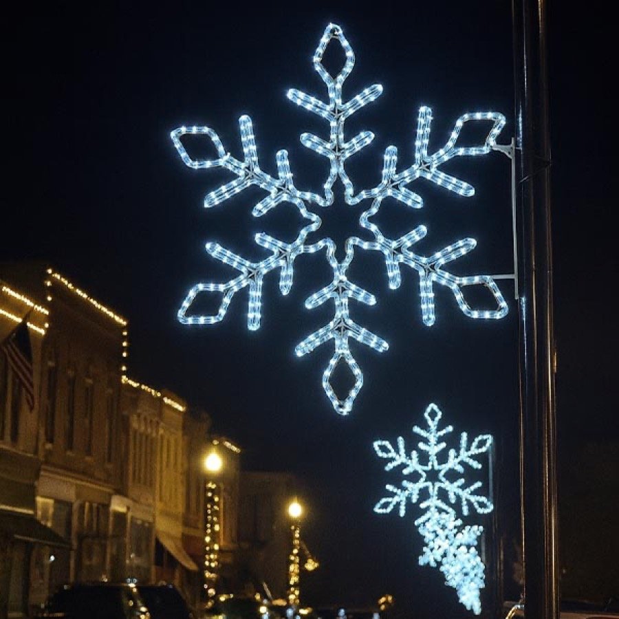 A blue and white lit snowflake mounted on a pole above a street.