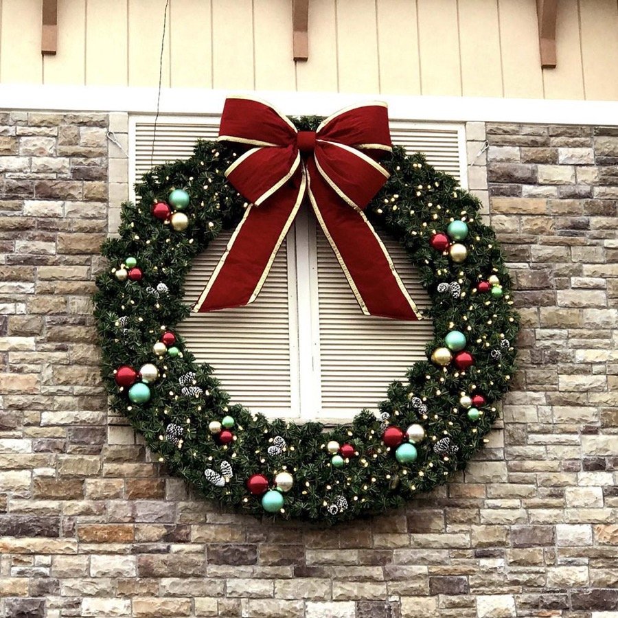 A large commercial wreath with a red bow mounted on a stone wall.