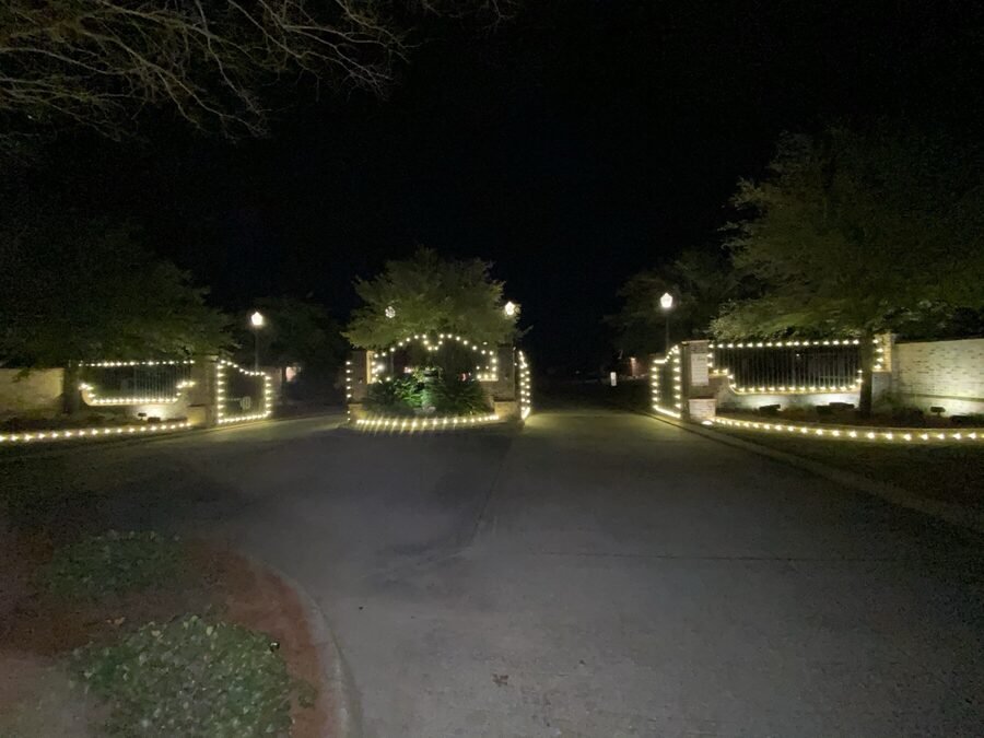 A gated property entrance at night with warm white lighting running along both entry walls.