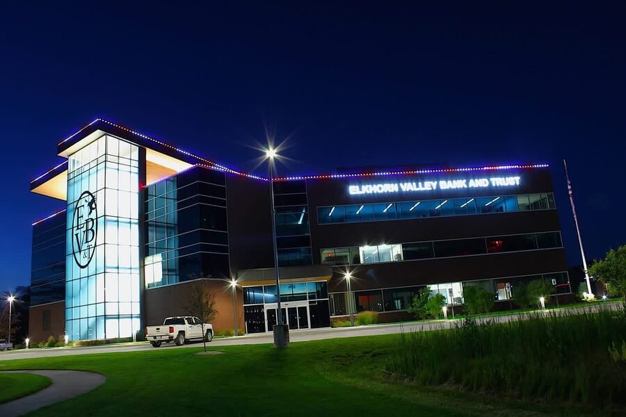 A four story bank headquarters at dusk with red, white and blue permanent lighting running the full roofline and parapet.
