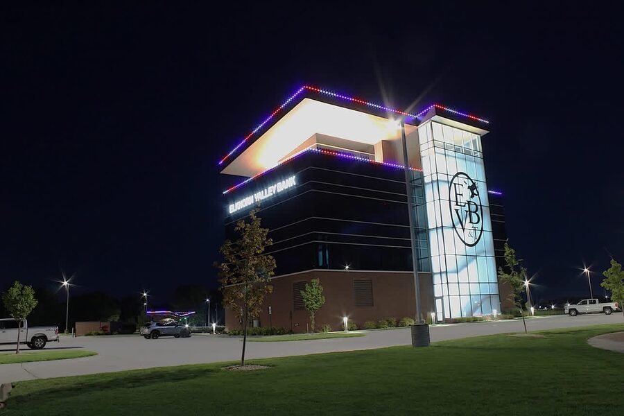 Side elevation of a modern bank building at dusk, permanent roofline lighting tracing the stepped parapet.