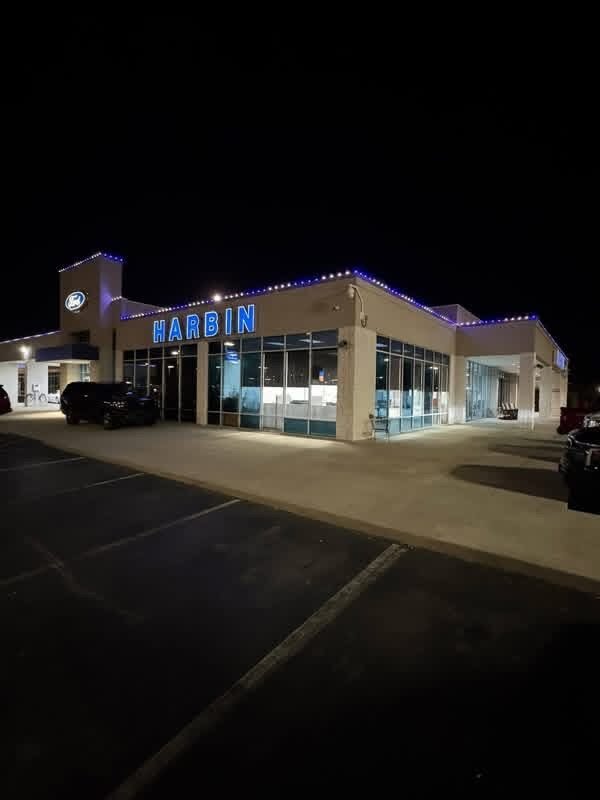 Close view of blue permanent lighting fixtures mounted along a dealership roofline at night.