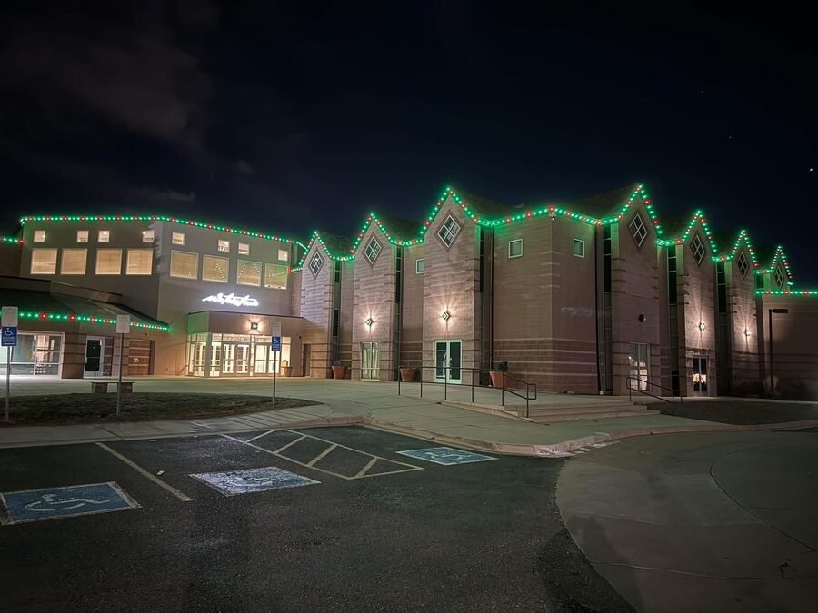 A large commercial building at night with permanent lighting set to alternating red and green across multiple gabled rooflines.