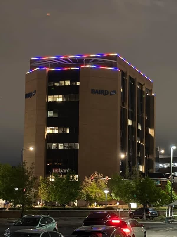 A multi story office tower at night with red, white and blue permanent lighting outlining the upper roofline and crown.