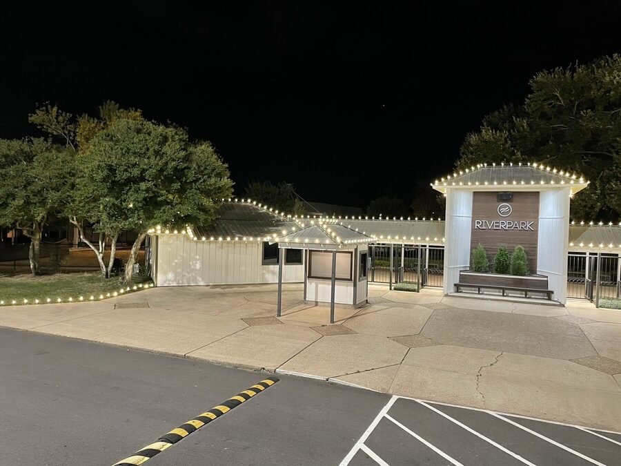 The lit entrance and covered walkway of a clubhouse at night, roofline traced in warm white.