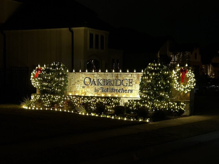A property entry monument decorated with lit wreaths, garland and red bows at night.